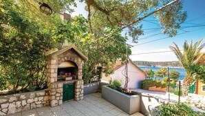 A stone-built outdoor kitchen with a green door, surrounded by lush greenery and overlooking a coastal view.