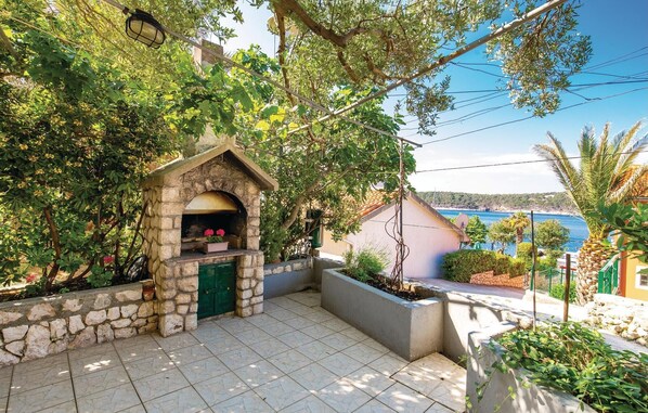 A stone-built outdoor kitchen with a green door, surrounded by lush greenery and overlooking a coastal view. - Cozy apartment in Barbat-Rab with WiFi (Barbat-Rab)