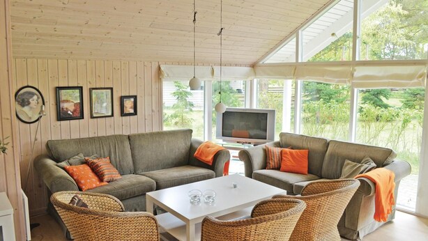 A cozy living room with a wooden ceiling, two grey sofas with orange cushions, a white coffee table, wicker chairs, and a television. - Awesome home in Væggerløse with sauna (Væggerløse)