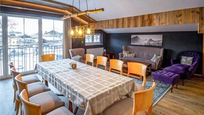 A dining area with a long table, multiple chairs, and a view of the city through large windows. - Ferienwohnung in Wagrain (Wagrain)