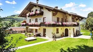A two-story building with balconies adorned with flowers, a well-maintained lawn, and a mountainous backdrop. - Ferienwohnung in Wagrain (Wagrain)