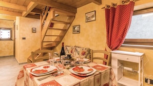Un comedor con una escalera de madera, una mesa dispuesta con platos y vasos, y un ventanal con cortinas rojas.