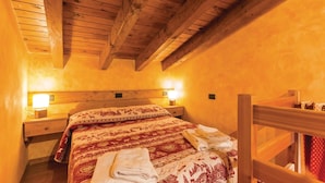 Un dormitorio acogedor con techo de madera, una cama con ropa de cama estampada, lámparas de noche y una mesita de noche de madera.