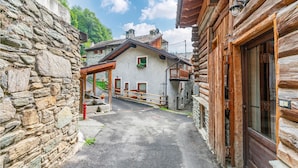 Una calle estrecha con edificios de piedra y casas de madera, con un muro de piedra a la izquierda y una casa de madera a la derecha.