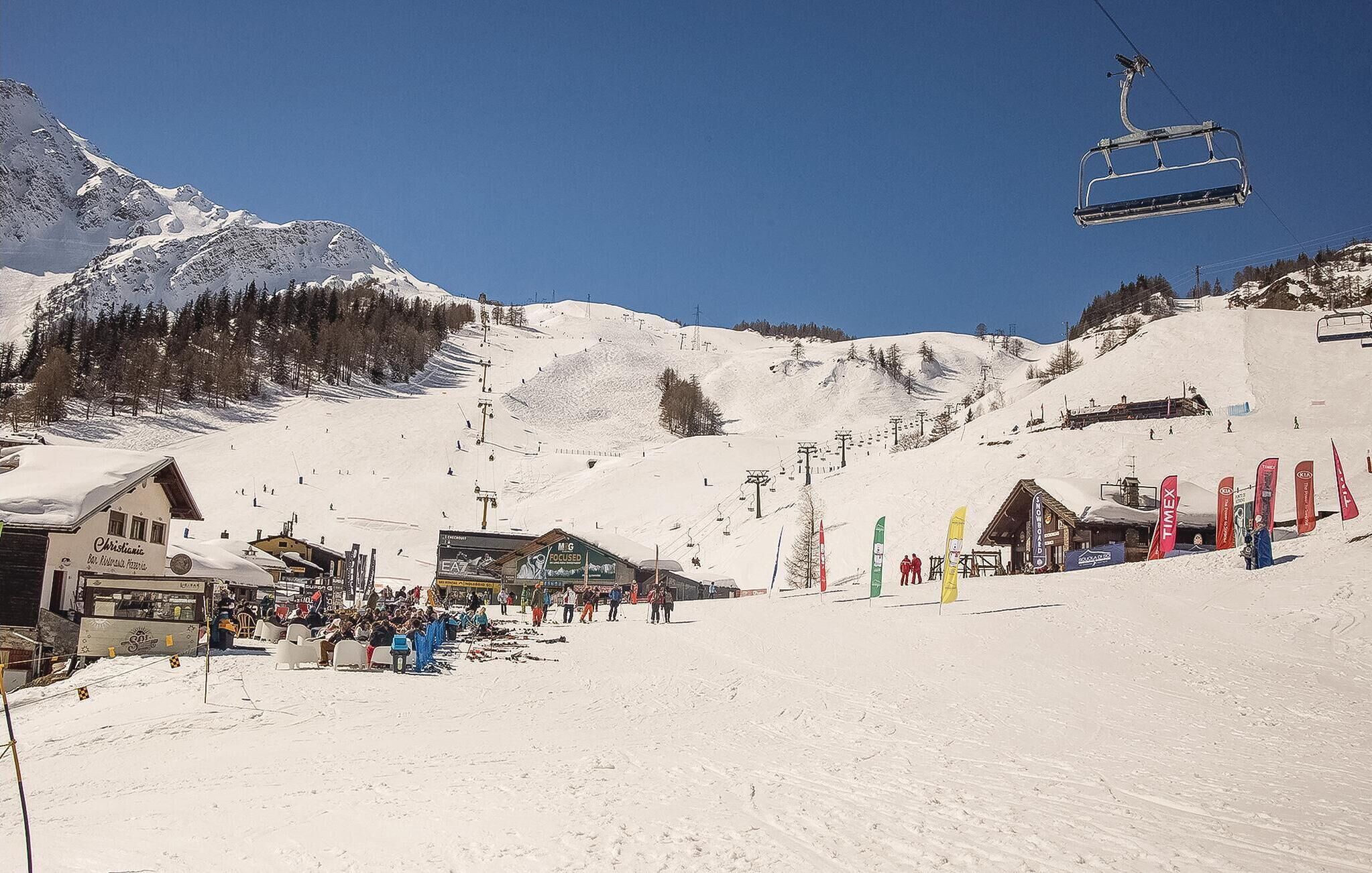 A ski resort with a chairlift, buildings, and a snowy mountain backdrop.
