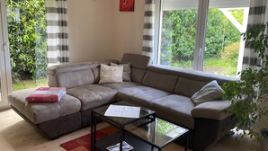 A modern living room with a sectional sofa, a glass coffee table, and a view of greenery through large windows.