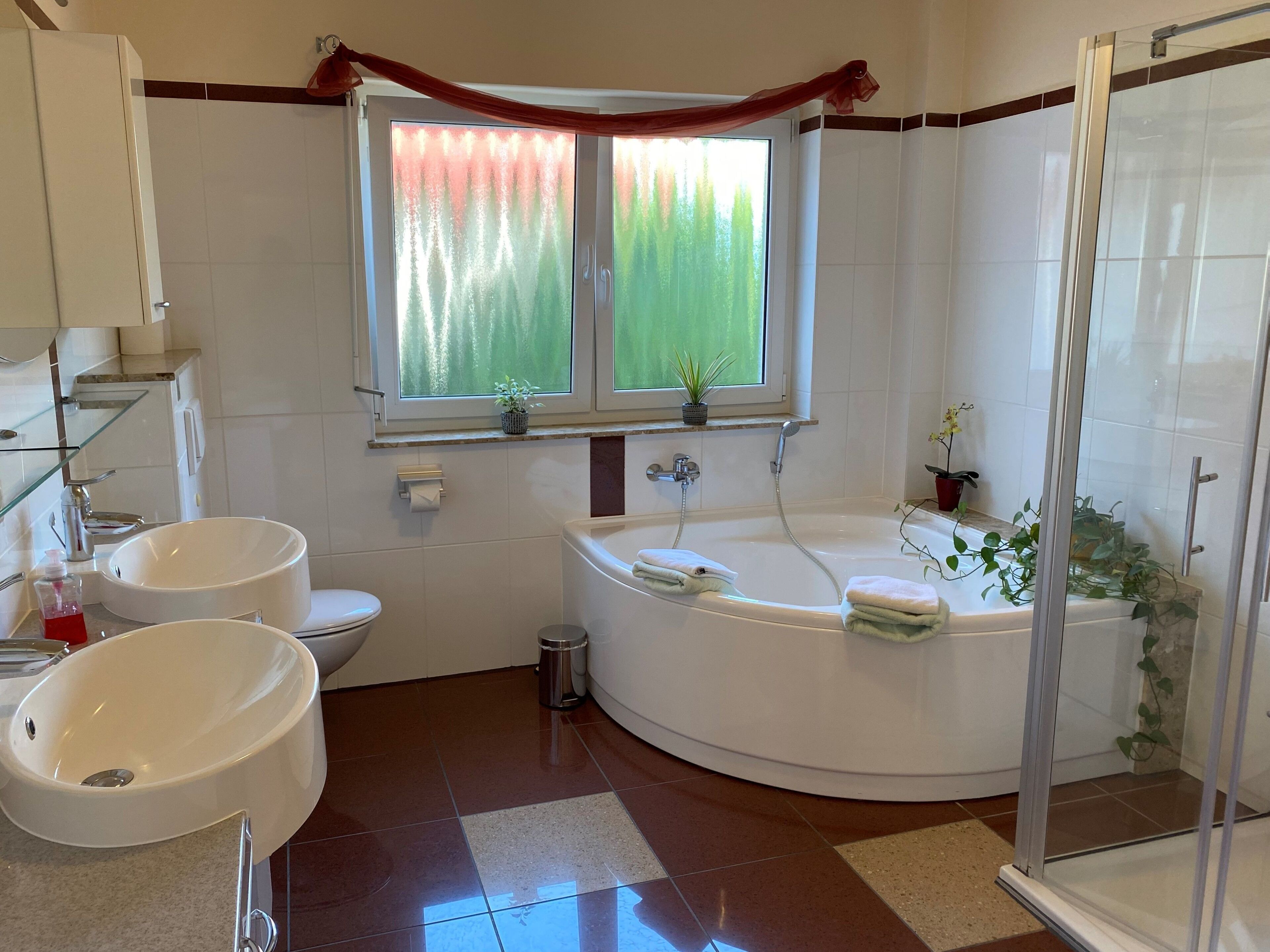 Un baño moderno con lavamanos doble, bañera, ducha y ventana con cortinas.