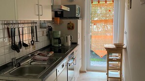 A kitchen with a sink, stove, and various utensils. There is a clock on the wall and a window with a curtain.