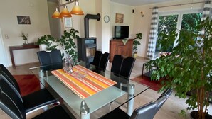 A modern dining area with a glass table, black chairs, and a striped table runner. There is a potted plant on the right and a fireplace in the background.