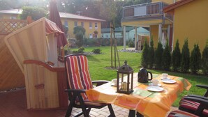 An outdoor patio with wicker furniture, a table set for tea, and a view of a yellow building and green lawn.