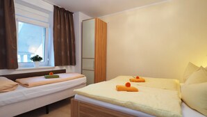A hotel room with two beds, a window with curtains, a small plant, and a mirror.