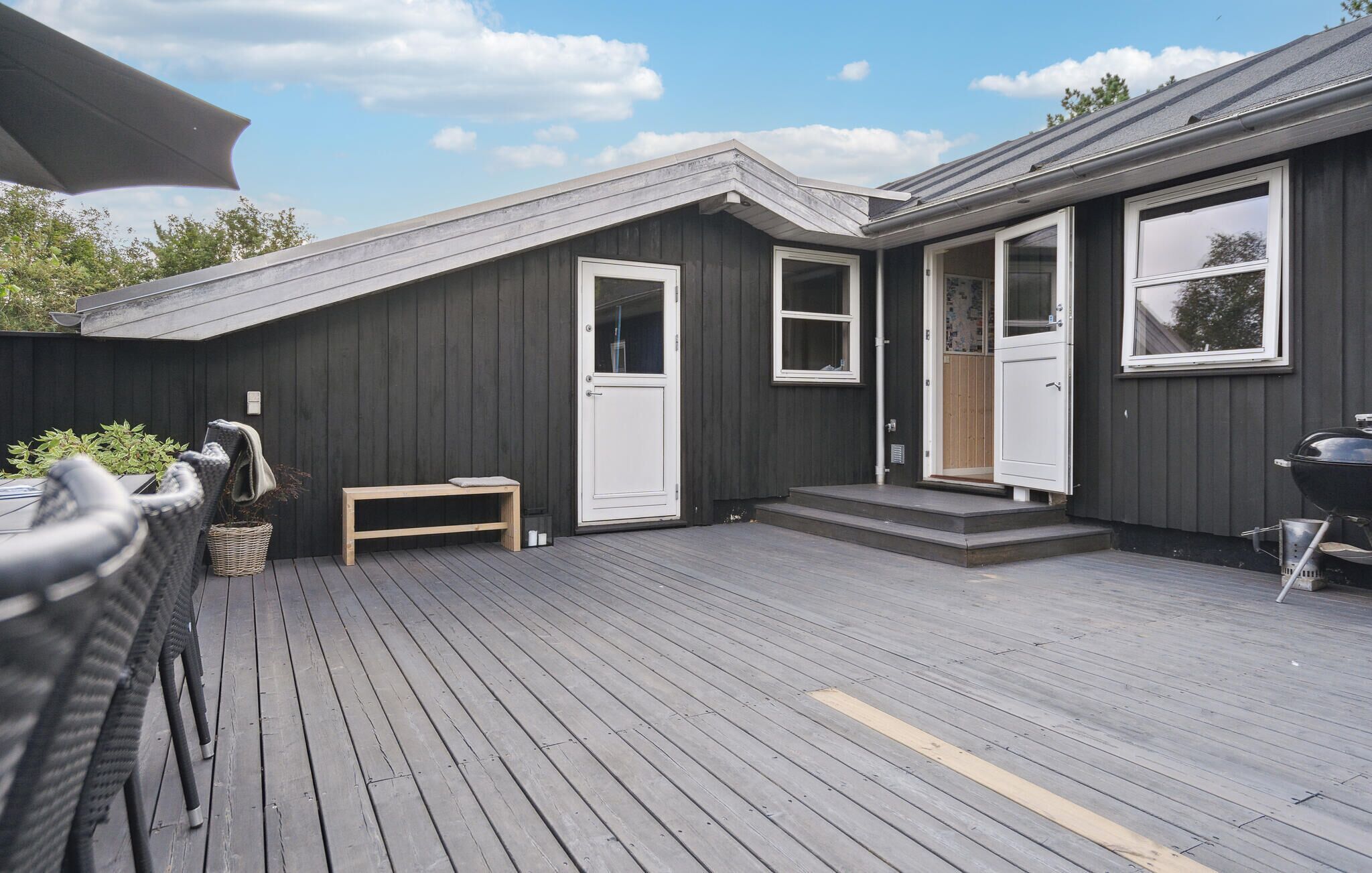 A wooden deck with a bench, a grill, and a door leading to a covered porch.
