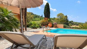 Area piscina con lettini, piscina e vista su un paesaggio collinare.