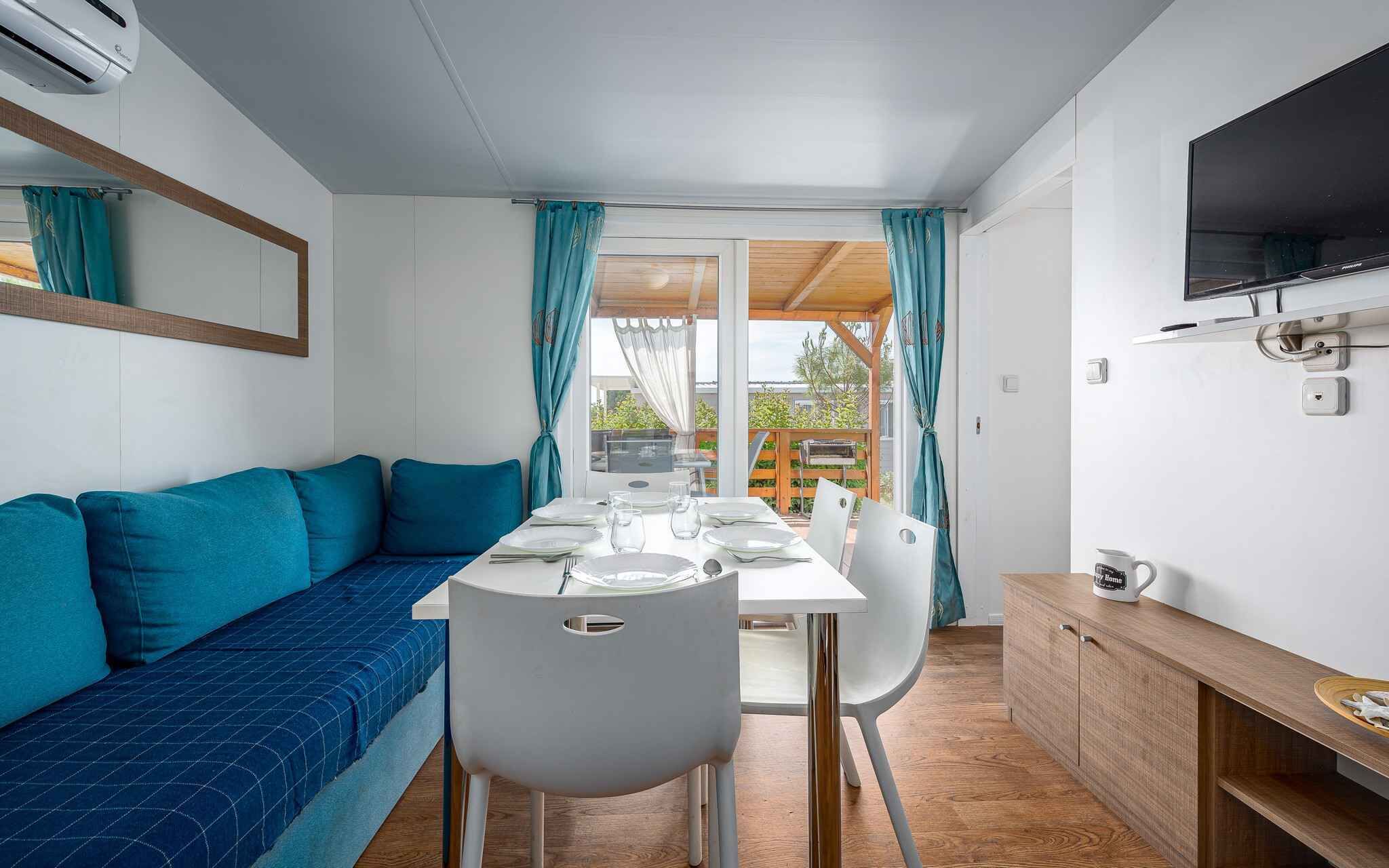A compact living space with a sofa, dining table, chairs, a TV, and a kitchenette.