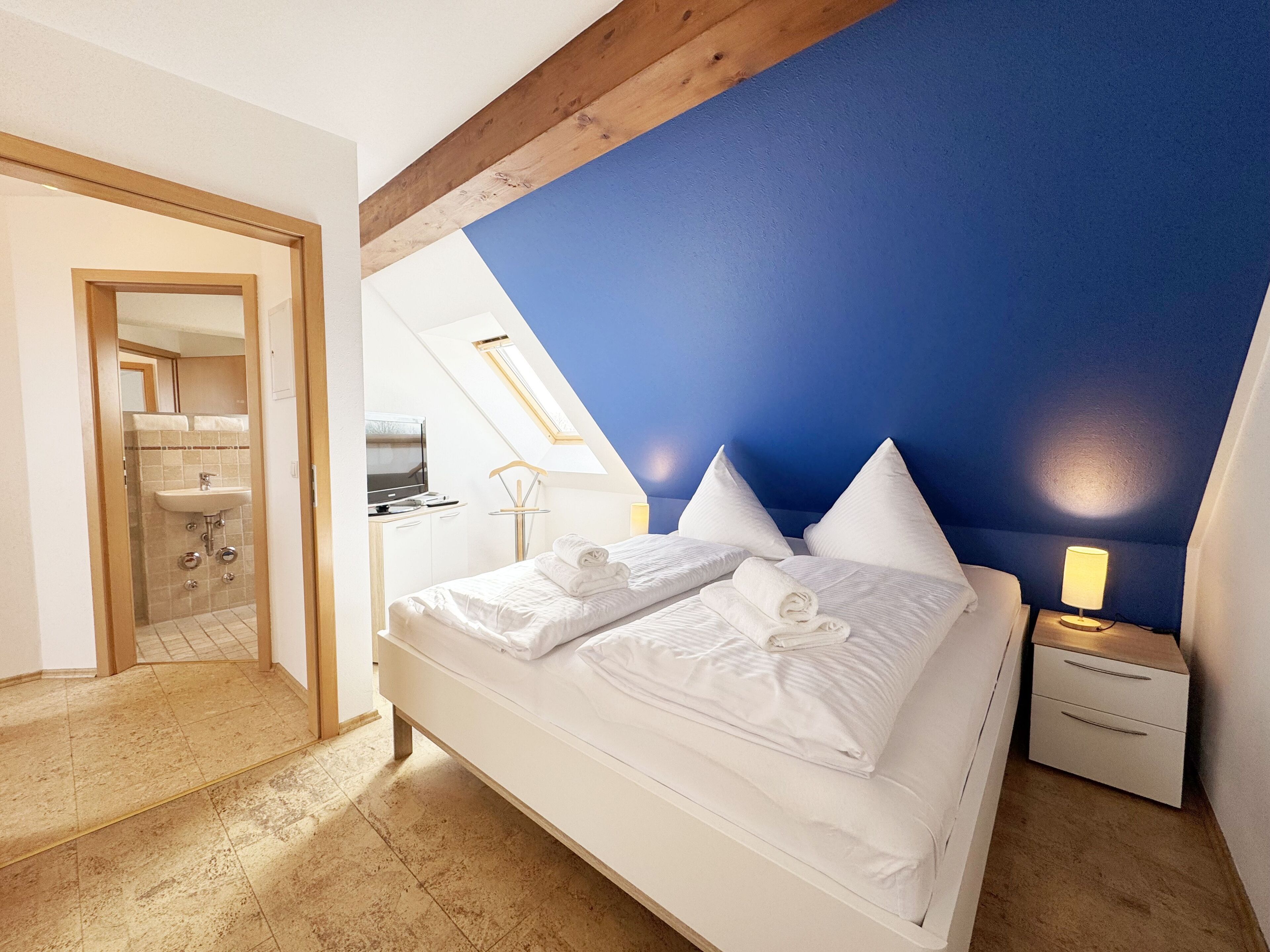 A bedroom with a bed, a nightstand, and a skylight.