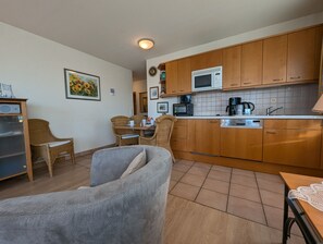 A compact kitchen with wooden cabinets, a microwave, a coffee maker, and a dining area with wicker chairs. - Oewern Diek 23, Germany (Wustrow)