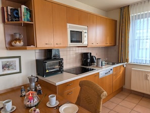 A kitchen with wooden cabinets, a microwave, a toaster, a coffee maker, and a dining table with chairs. - Oewern Diek 23, Germany (Wustrow)