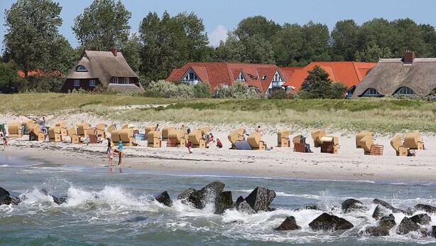 Ein Strand mit reetgedeckten Hütten und Liegestühlen.