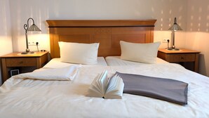 Ein ordentlich bezogenes Bett mit Kissen, Decke und einem offenen Buch, zwei Nachttischlampen und einem Holz-Kopfteil.