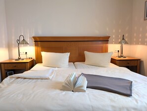 Ein ordentlich bezogenes Bett mit Kissen, Decke und einem offenen Buch, zwei Nachttischlampen und einem Holz-Kopfteil.