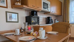Eine Küche mit Holzausstattung, einer Mikrowelle, einer Kaffeemaschine und einem Esstisch, gedeckt mit Tellern, Tassen und Besteck.