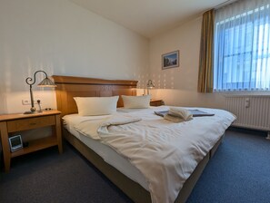 A hotel room with a bed, bedside tables, lamps, a picture on the wall, and a window with curtains. - Oewern Diek 23, Germany (Wustrow)