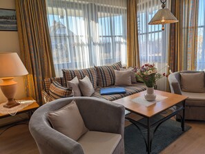Ein gemütliches Wohnzimmer mit einer Couch, Sesseln, einem Couchtisch und einer Lampe.