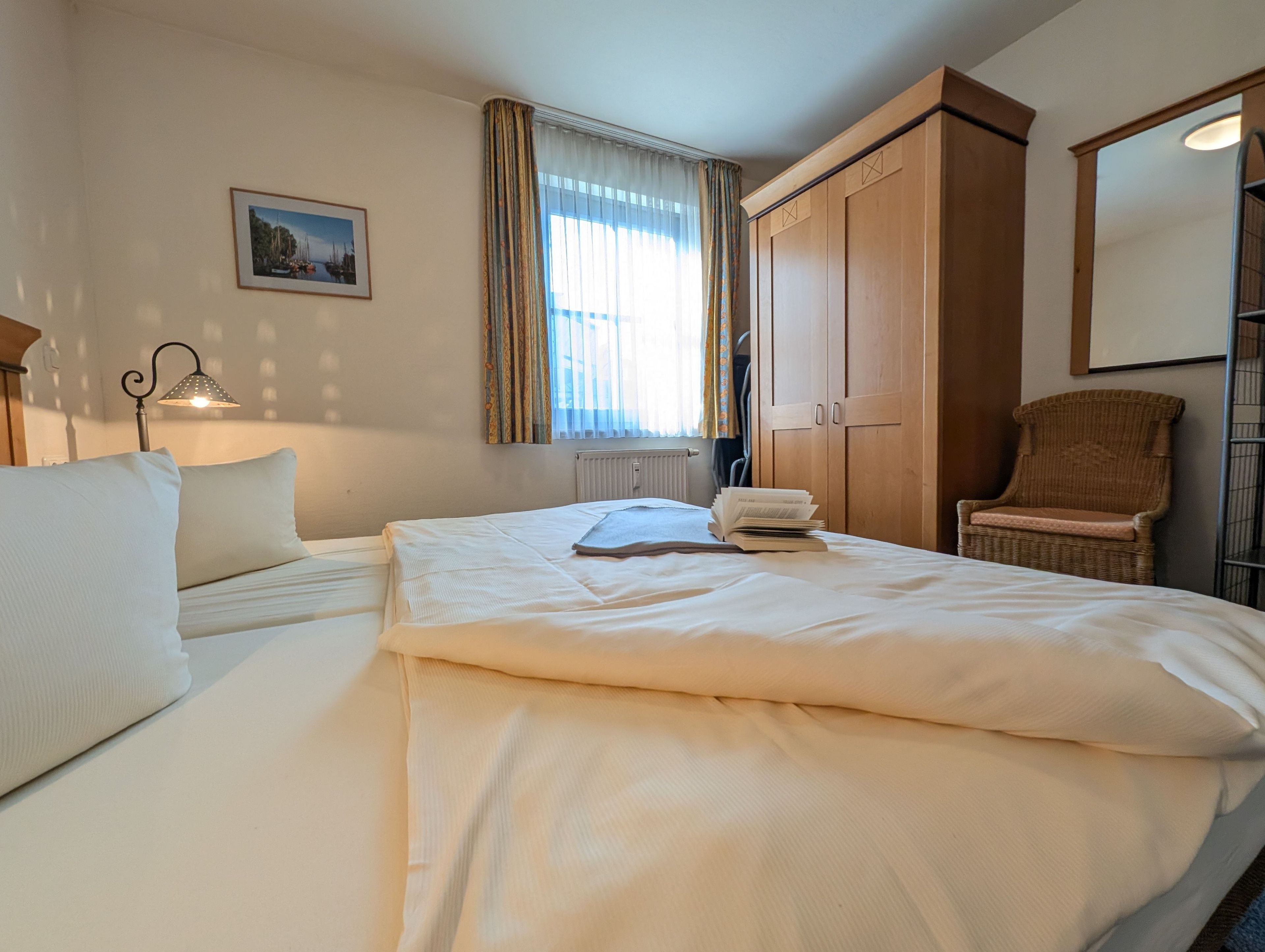 Une chambre d’hôtel avec un lit, une chaise, une armoire, un radiateur et un tableau au mur.