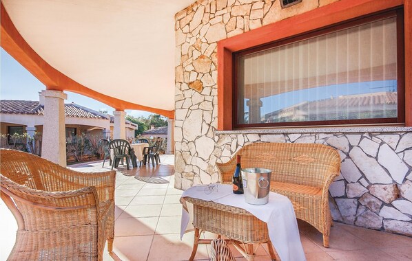 Un patio con mobiliario de mimbre, una mesa y un muro de piedra.