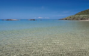 Una playa despejada con aguas poco profundas, afloramientos rocosos y una costa distante.
