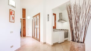 A hallway with a kitchen area, including a stove, oven, and dishwasher. There are wooden doors and a vase with branches. - 3 bedroom cozy home in Costa Rei -CA- (Costa Rei -CA-)
