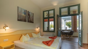Habitación de hotel con una cama grande, dos mesitas de noche, una ventana con cortinas y vista a la calle.