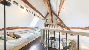 A cozy attic bedroom with a sloped ceiling, exposed wooden beams, a bed with pillows, a small table, and a bookshelf. - Nice apartment in Ocquerre with swimming pool (Ocquerre)
