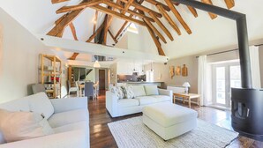 A spacious living area with a high ceiling and exposed wooden beams, a cozy seating area with a sofa and ottoman, a kitchen in the background, and a large fireplace. - Nice apartment in Ocquerre with swimming pool (Ocquerre)