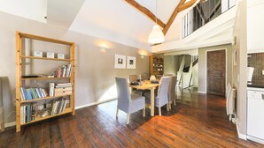 A spacious dining area with a wooden table and chairs, a bookshelf, and a staircase leading to an upper level. - Nice apartment in Ocquerre with swimming pool (Ocquerre)