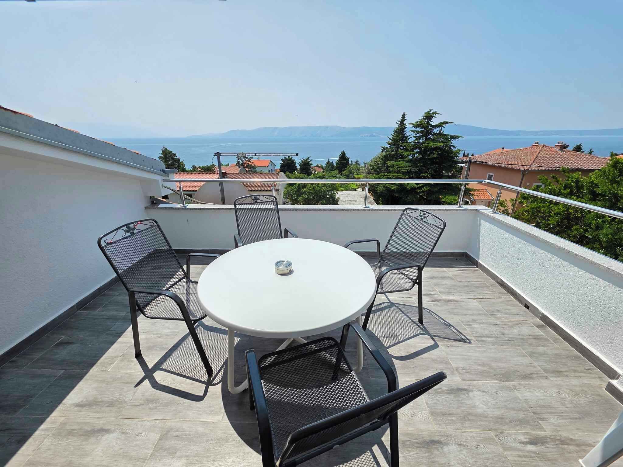 Ein runder Tisch mit vier Stühlen auf einem Balkon mit Blick auf das Meer und die entfernten Hügel.
