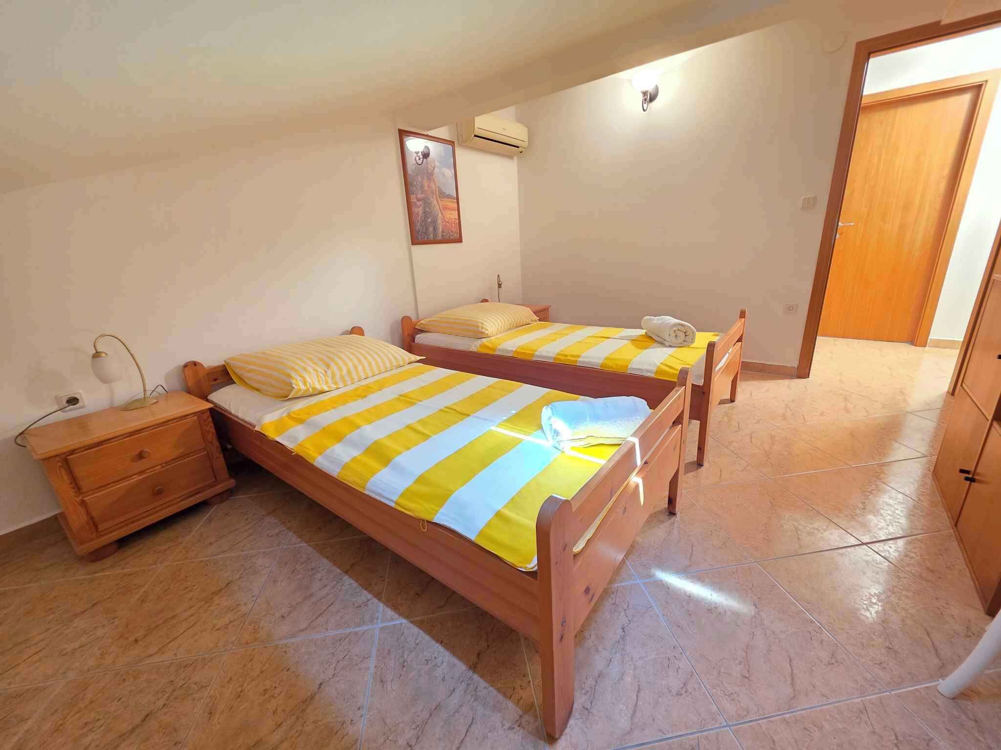 Una camera da letto con due letti in legno, un comodino, un condizionatore d'aria a muro e una porta che dà su un'altra stanza.