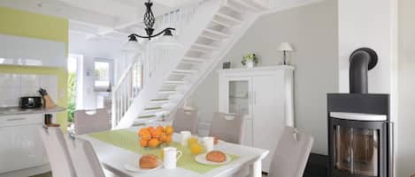 Une cuisine moderne avec un coin repas, des meubles blancs, un escalier et un poêle à bois.