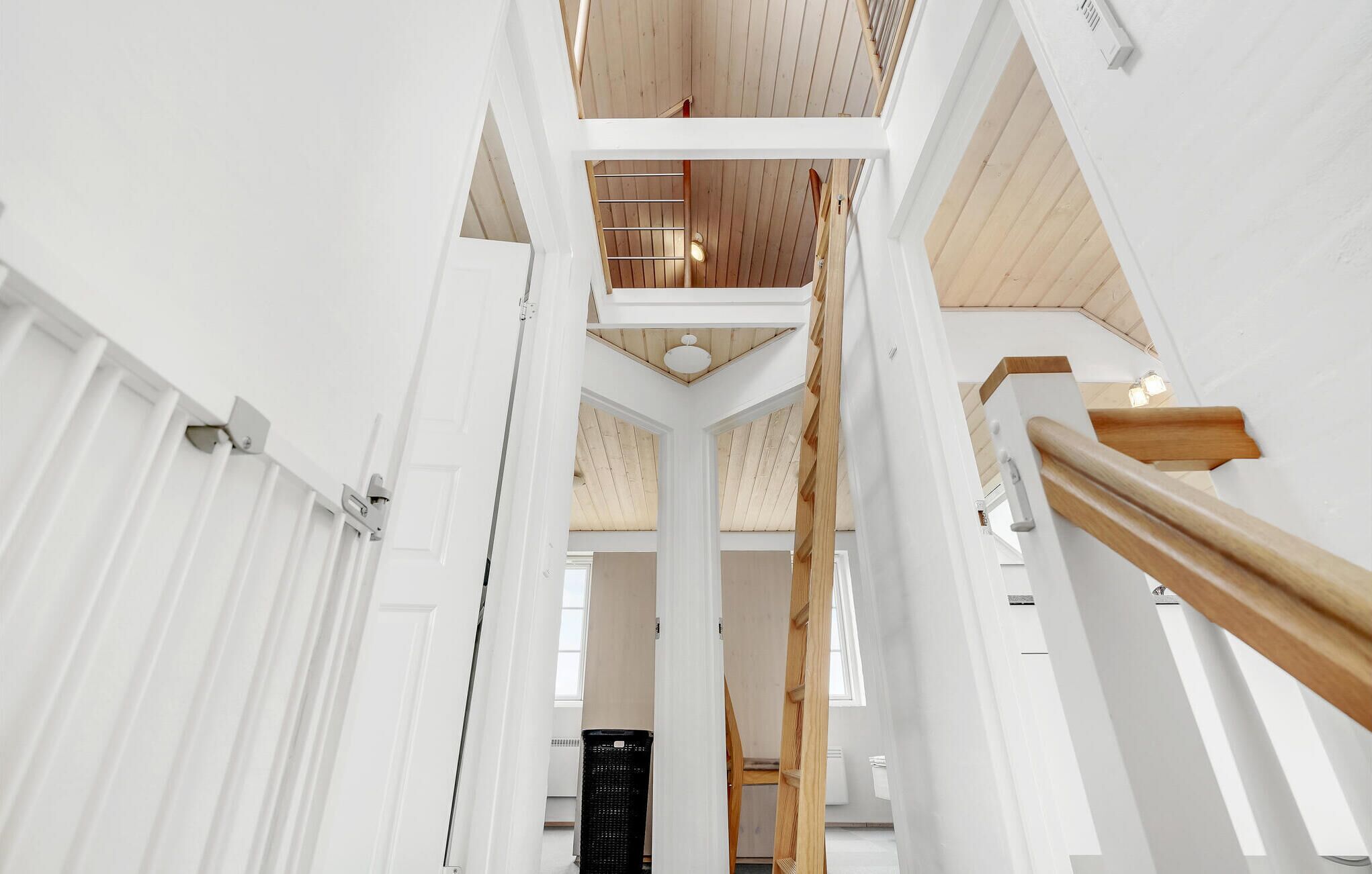 Ein mehrgeschossiges Interieur mit weißen Wänden, Holzbalken und einer zentralen Treppe.