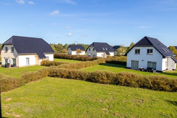 A row of white houses with dark roofs, surrounded by well-maintained hedges and grass.