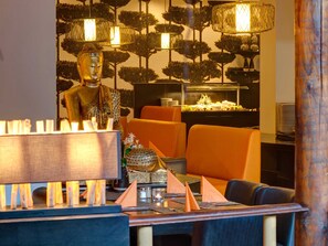 A restaurant with a Buddha statue, orange chairs, a buffet, and a patterned wall.