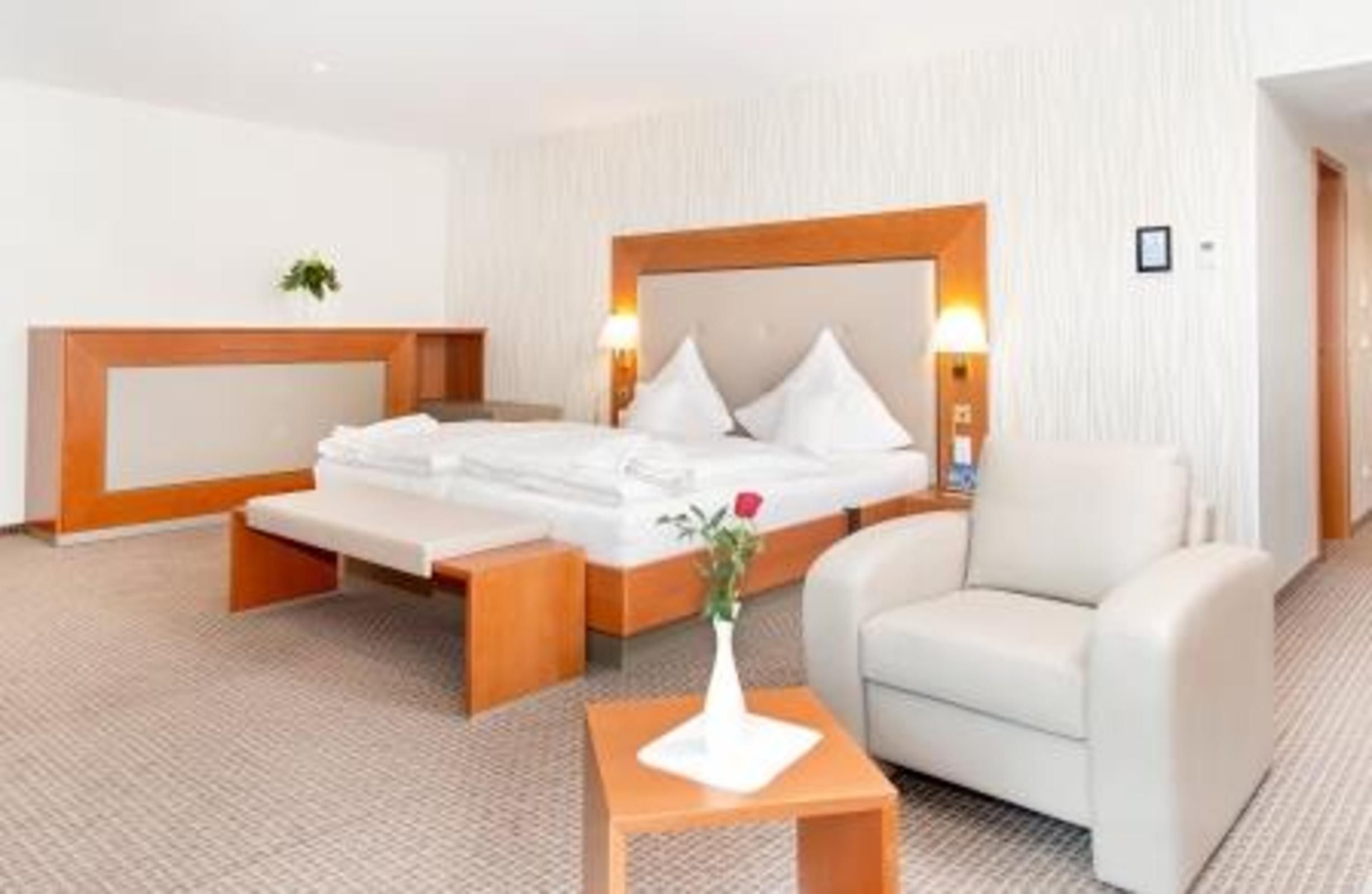 Ein Hotelzimmer mit einem Bett, einem Nachttisch, einem Sessel und einem kleinen Tisch mit einer Vase.