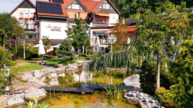A hotel with a pond, surrounded by lush greenery and a red-roofed building. - Deluxe Double Room - Hotel Teutoburg Forest GmbH (Tecklenburg)