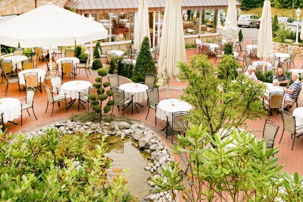 An outdoor patio with round tables and chairs, a small water feature, and a view of the restaurant in the background.