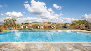 Ein Pool mit Liegestühlen und Sonnenschirmen, umgeben von einem Holzzaun und Steinplatten.