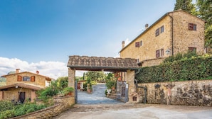 Ein Steinhaus mit überdachter Eingangspforte, einem gepflasterten Weg, der zu einem Tor führt, und einem Garten mit Kübelpflanzen.