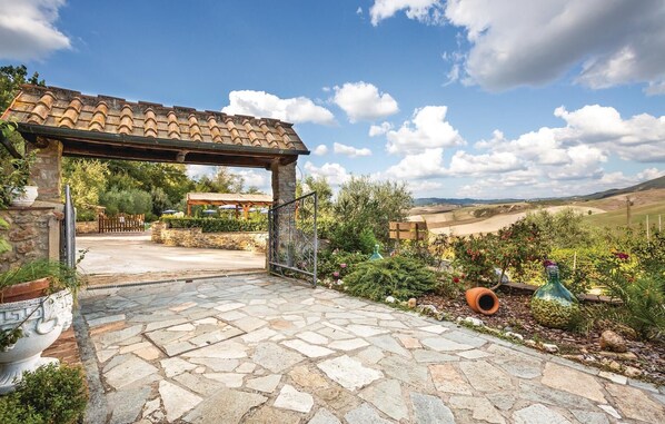 A stone-paved patio with a pergola, stone walls, and a view of rolling hills.