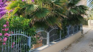 A residential building with a balcony, surrounded by lush greenery and flowering plants.