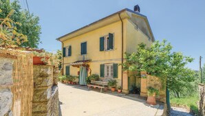 A two-story yellow building with green shutters, a stone wall on the left, and potted plants in front. - Cozy home in Valpromaro-Camaiore LU (Valpromaro-Camaiore LU)