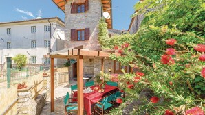 A stone building with a red-tiled roof, a wooden pergola, and a table set for dining. - Cozy home in Valpromaro-Camaiore LU (Valpromaro-Camaiore LU)